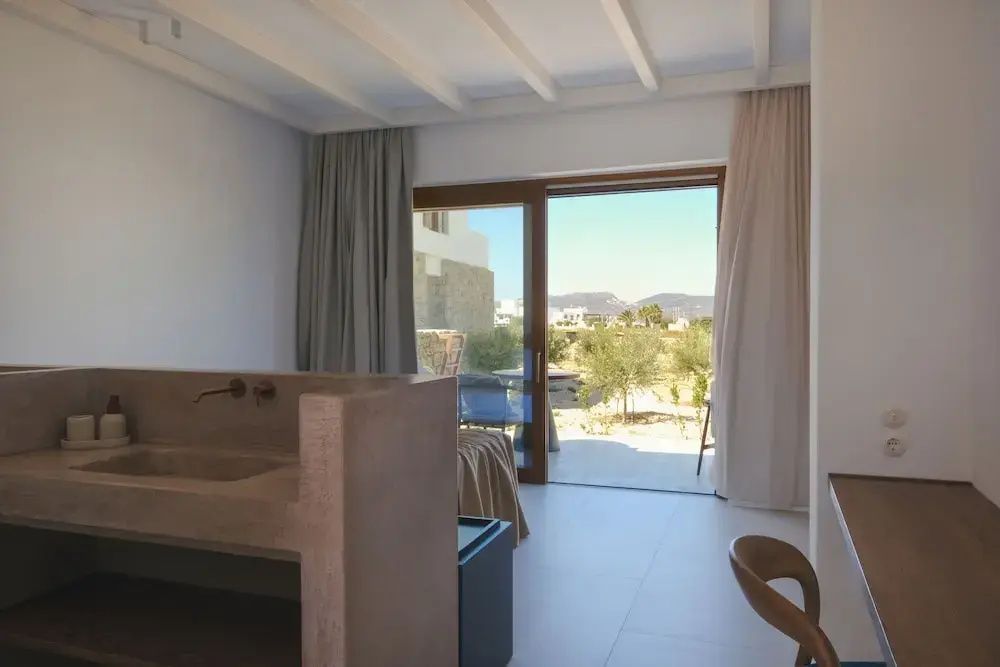 Helles Hotelzimmer mit Blick durch die Glas-Schiebetür auf die sonnige Terrasse und Natur.