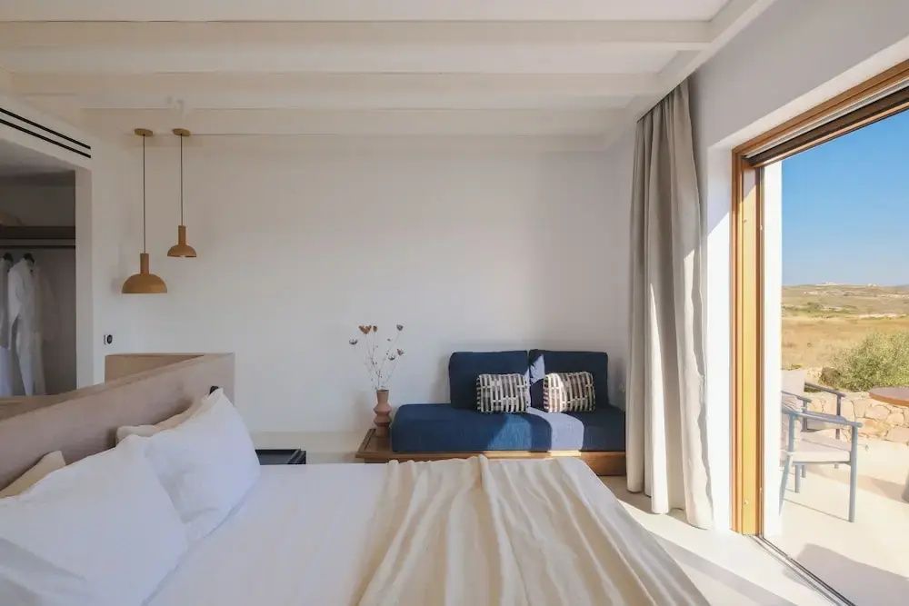 Helles Hotelzimmer mit Doppelbett, blauem Sofa und Vorhang neben der Terrassentür.