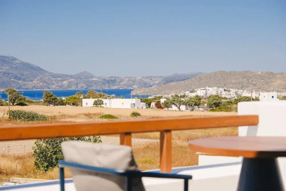 Blick von der Terrasse über trockene Felder auf das blaue Meer und die Hügelkette.