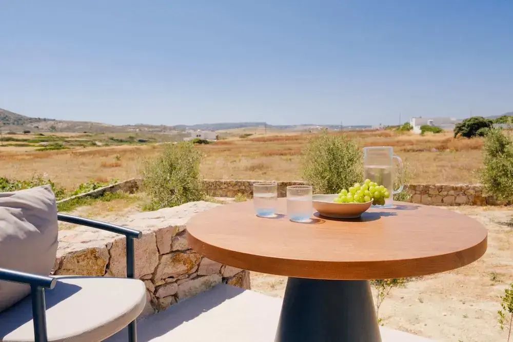 Runder Holztisch auf der Terrasse mit Trauben und Wassergläsern vor weiter Landschaft.