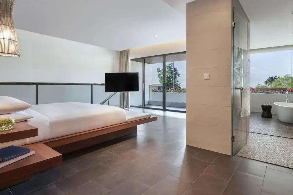 Offenes Schlafzimmer mit Holzplattform Bett, Fernseher und Zugang zu einem Balkon.