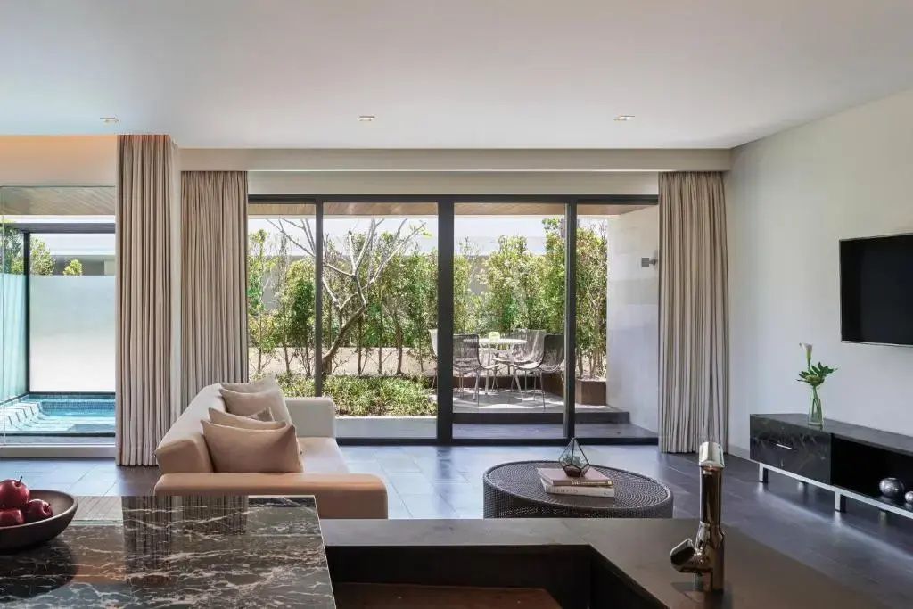 Wohnbereich einer Suite mit hellem Sofa, Couchtisch und Blick auf die grüne Terrasse.
