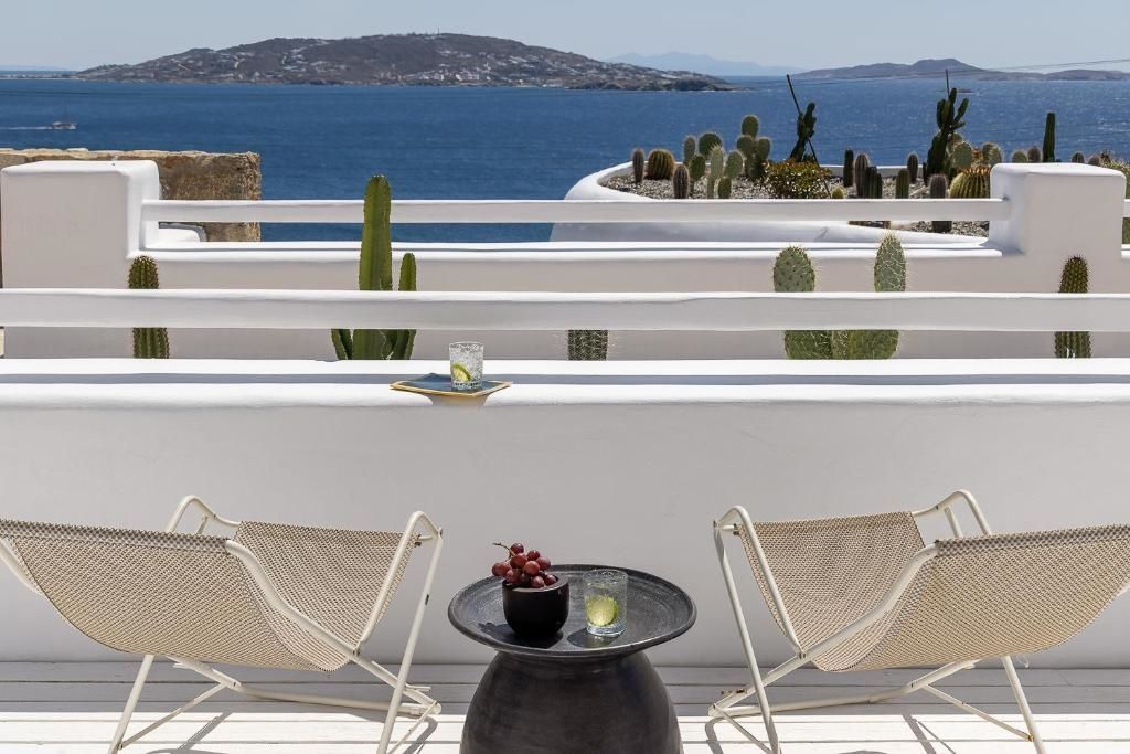 Terrasse mit Stühlen und Tisch mit Blick auf das blaue Meer und die Nachbarinsel.