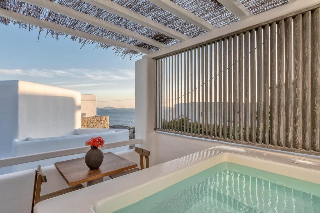Terrasse mit Whirlpool, kleinem Holztisch und Blick auf das Meer unter einer Überdachung.