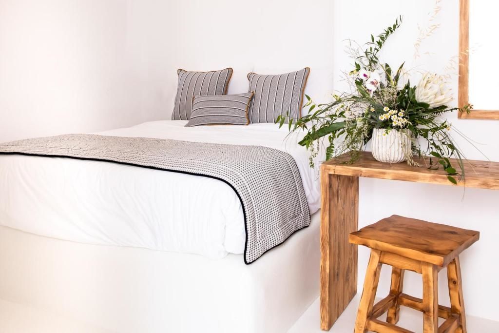 Doppelbett mit gestreiften Kissen, Holzkonsole und einem Holzhocker in weißem Raum.