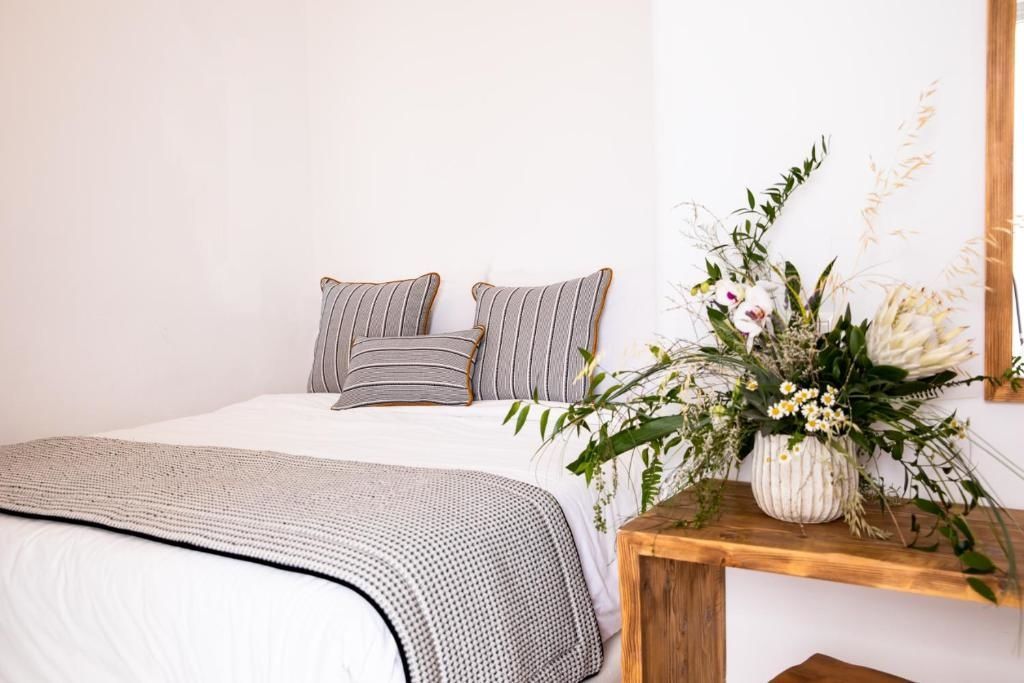 Weiss bezogenes Bett mit gestreiften Kissen und ein Holztisch mit Blumenschmuck.