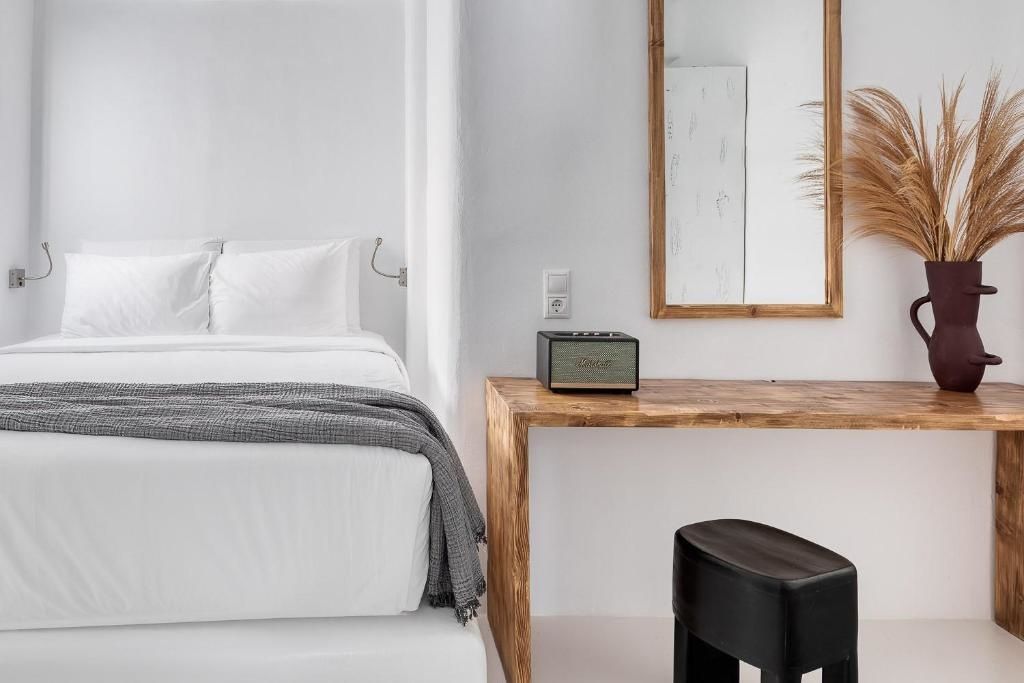 Weißes Bett neben einer Holzkonsole mit Spiegel und Musikbox in hell gestaltetem Zimmer.