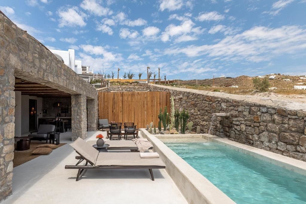 Privater Poolbereich mit Sonnenliegen, Natursteinmauer und Kakteen unter blauem Himmel.