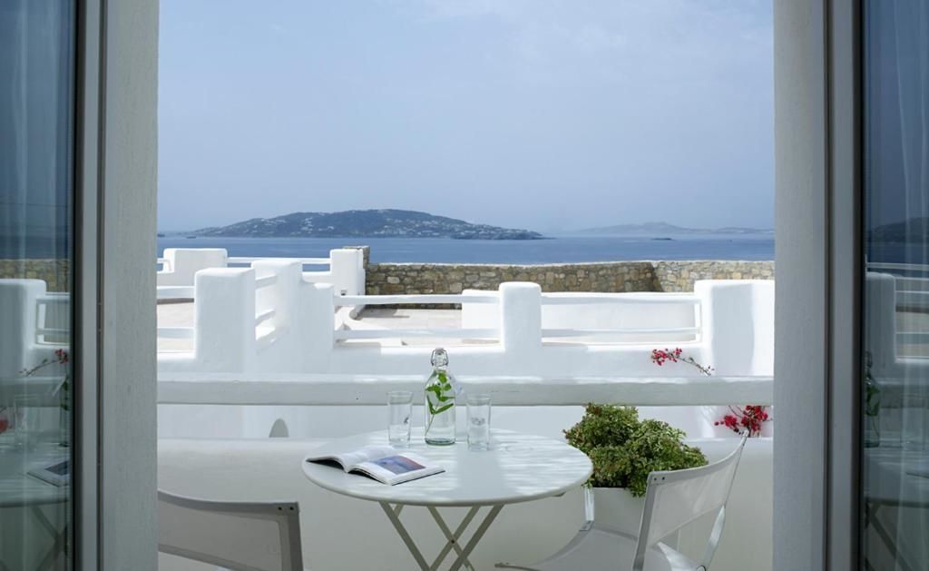 Kleine weiße Terrasse mit einem Tisch, zwei Stühlen und Gläsern vor der Kulisse des blauen Meeres.