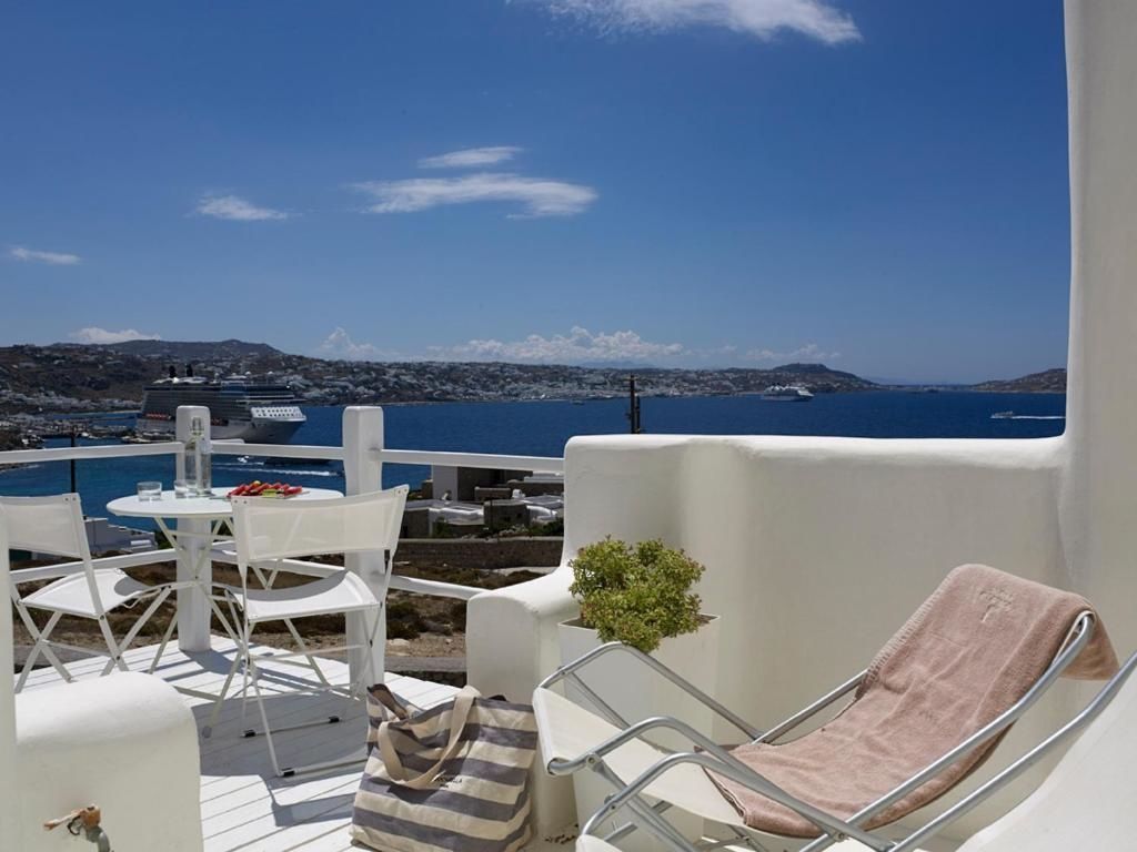 Weiße Terrasse mit Stühlen, Liegestuhl und Strandtasche mit Blick auf das blaue Meer.