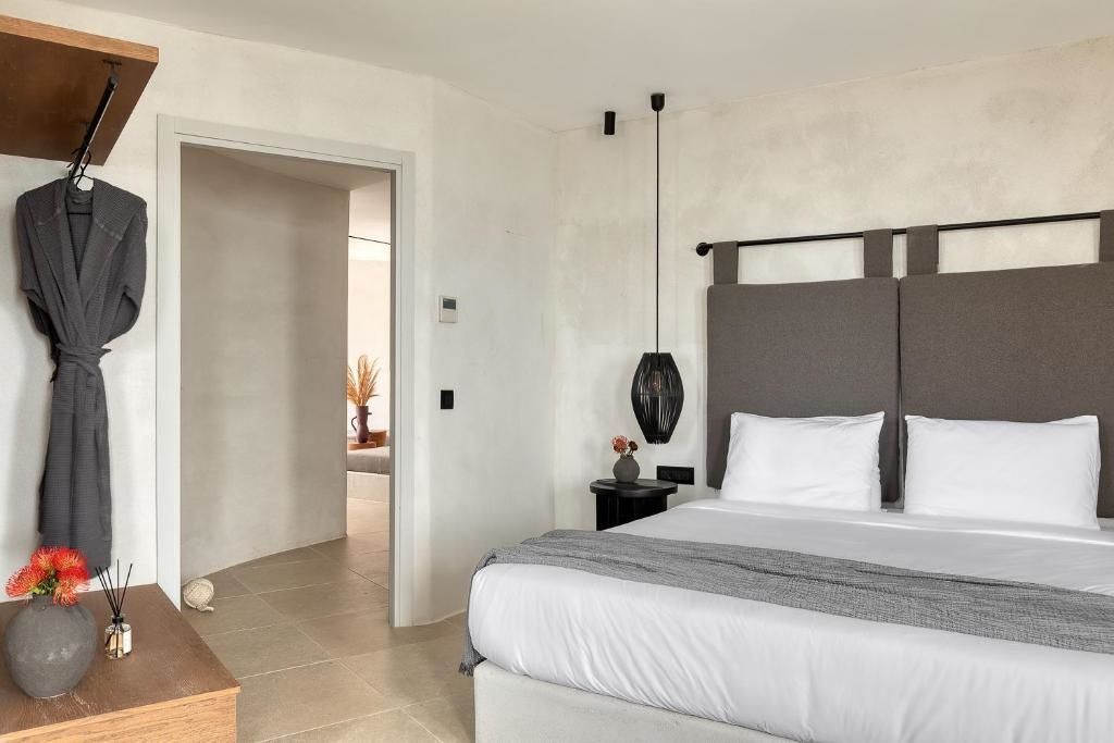 Helles Hotelzimmer mit Doppelbett, grautönigem Kopfteil und Blick in den Nachbarraum.
