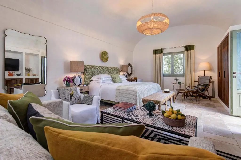 Helles Schlafzimmer mit grün verziertem Bett, Sesseln und Rattanlampe.