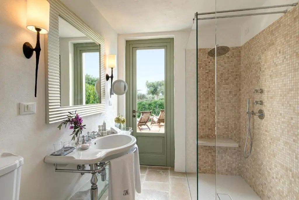 Badezimmer mit Waschbecken, Glasdusche und Blick auf die sonnige Terrasse.