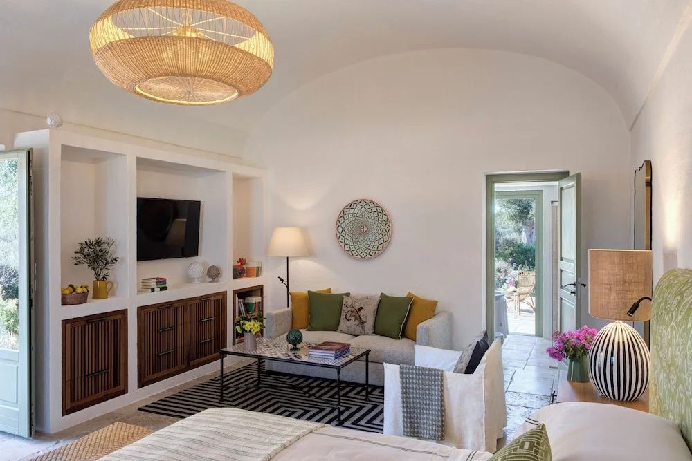 Wohnbereich einer Suite mit hellem Sofa, bunten Kissen, Couchtisch und Wandfernseher.