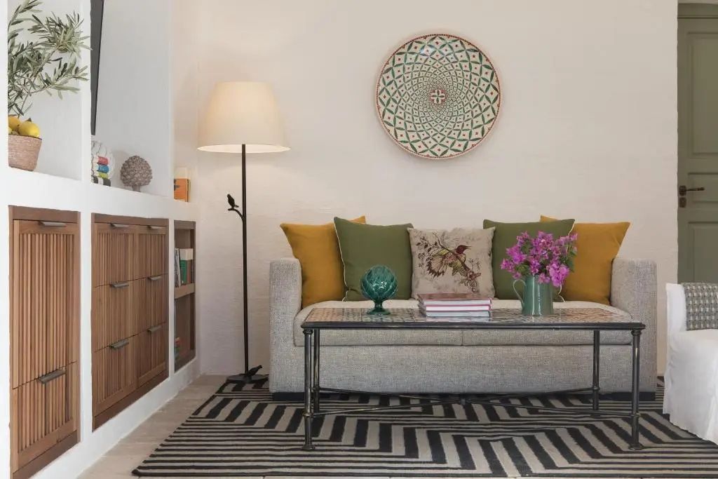 Sitzbereich mit grauem Sofa, Kissen, Wanddekoration und schwarzer Stehlampe.