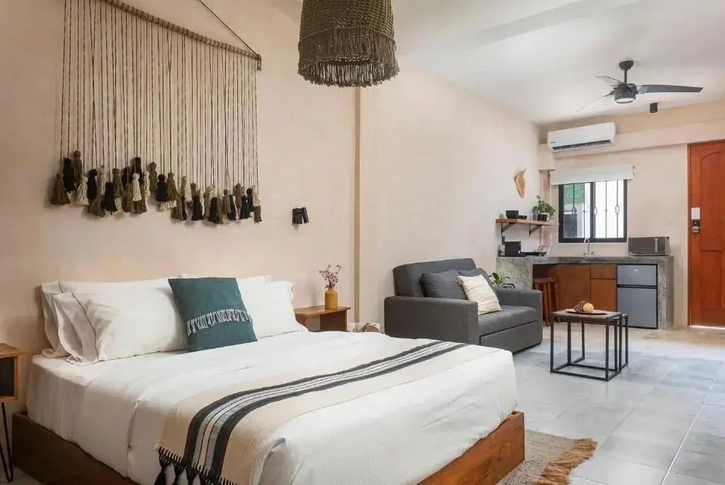 Kombinierter Wohnbereich und Schlafbereich mit Doppelbett, dunklem Sofa und Küchenzeile.