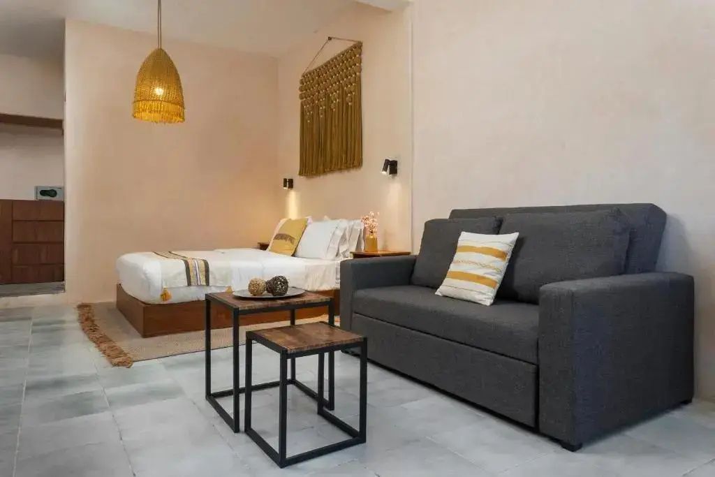 Graues Sofa mit Holztischen im Vordergrund und Doppelbett im hinteren Raumbereich.