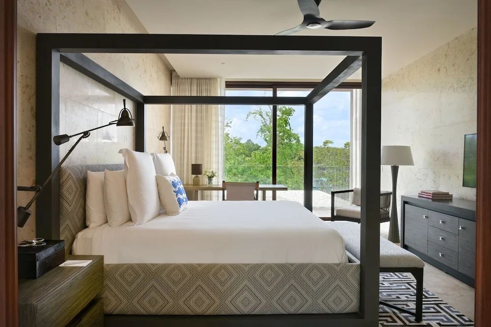 Schlafzimmer mit dunklem Himmelbett, weißer Bettwäsche und Blick ins Grüne.