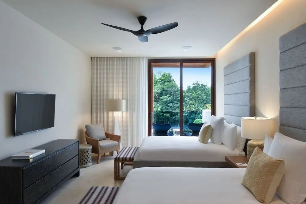 Hotelzimmer mit zwei Doppelbetten, Sessel und Glasfront zum Balkon im Grünen.