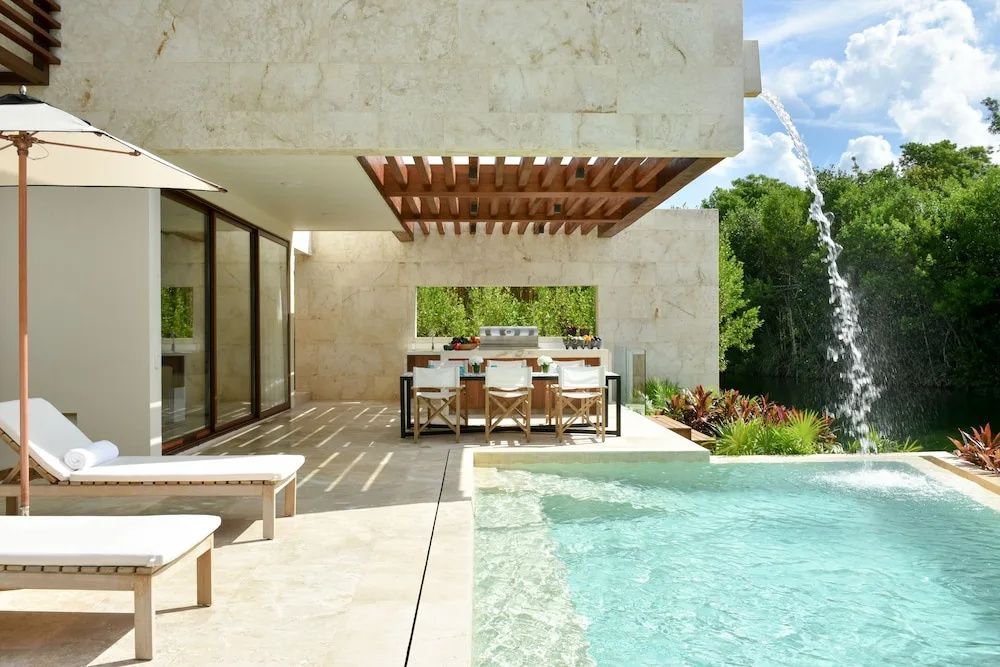 Terrasse einer Villa mit Privatpool, Outdoor-Küche und Esstisch unter einer Holzpergola.