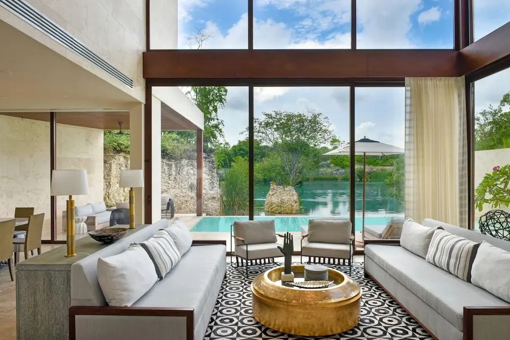 Wohnzimmer mit großen Fenstern, hellem Sofa und Blick auf den Pool an der Lagune.