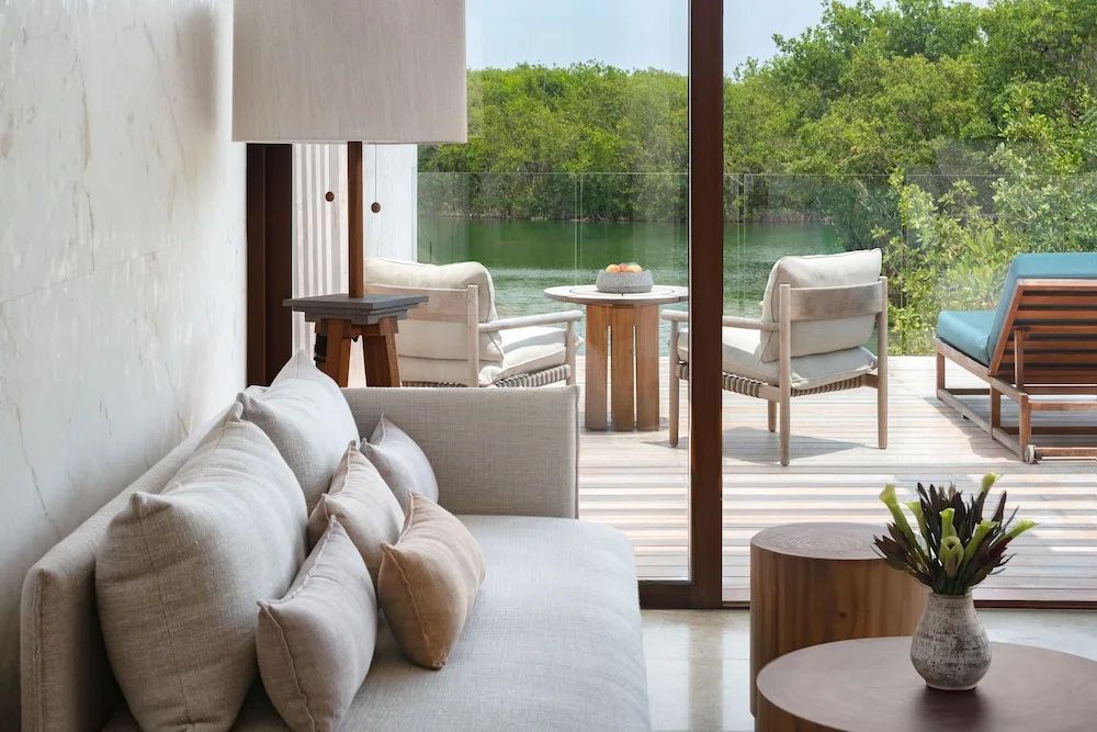 Sitzbereich im Zimmer mit Blick durch die Glasfront auf Terrasse und Lagune.