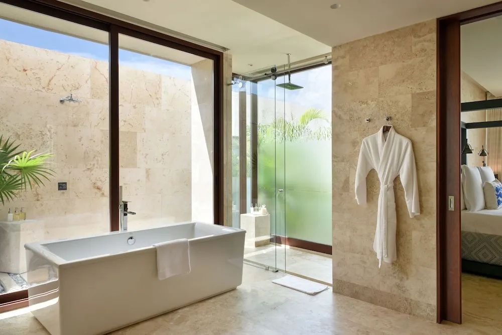 Badezimmer mit freistehender weißer Wanne, Glasdusche und Wänden aus Naturstein.