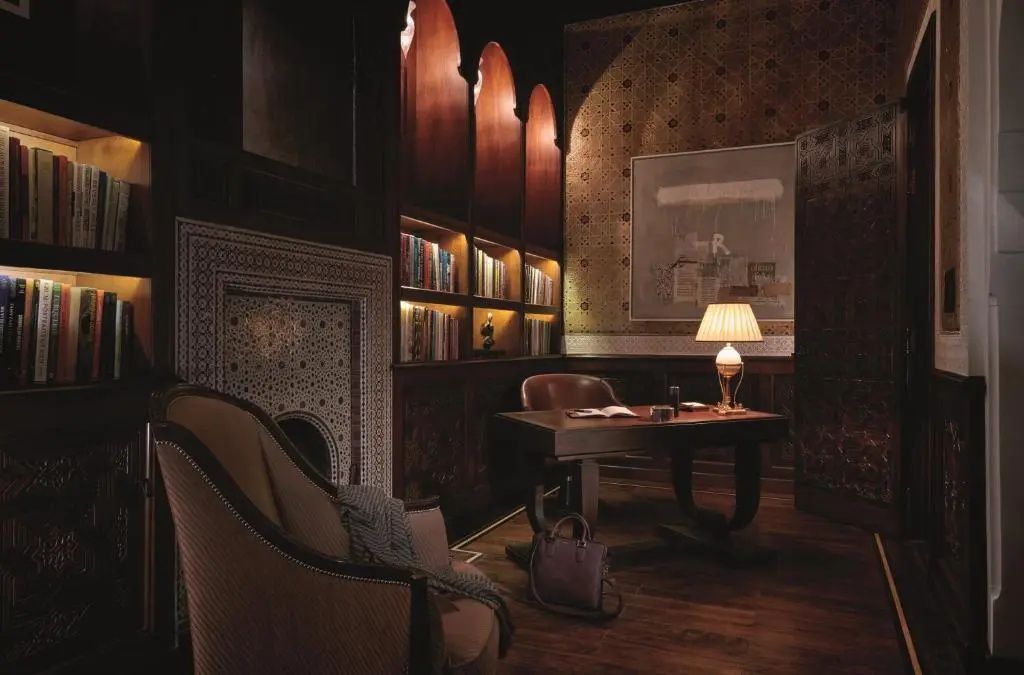 Schreibtisch mit Tischlampe, Armlehnenstuhl und beleuchtetem Bücherregal im Wohnbereich.
