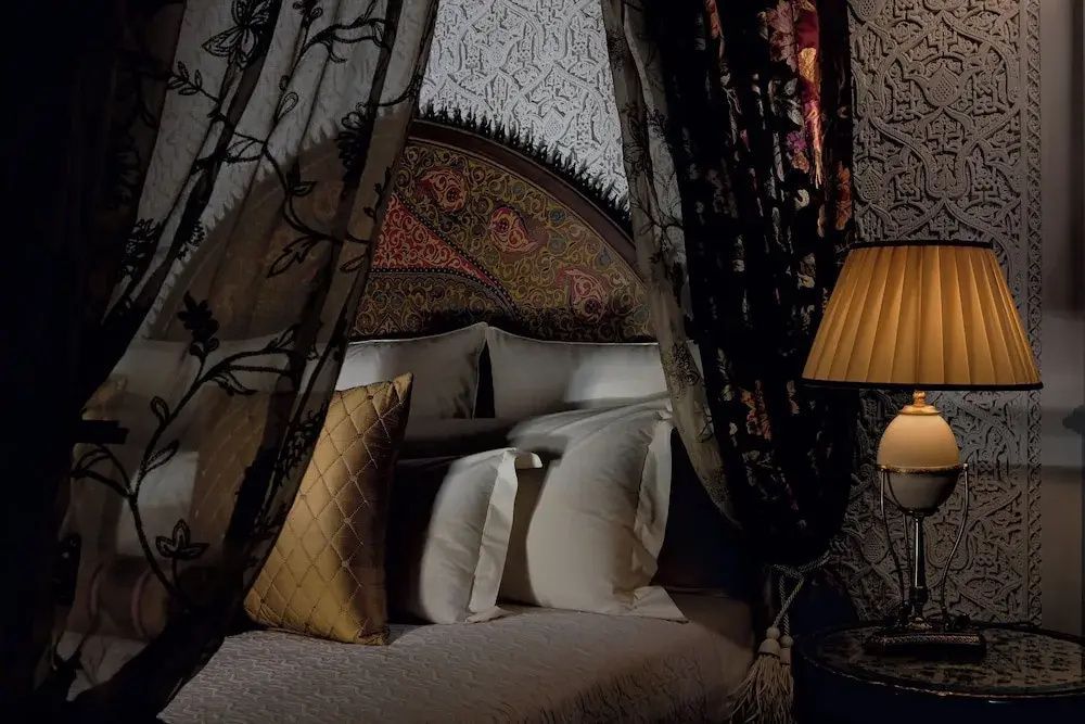 Doppelbett mit verziertem Kopfteil, Vorhängen und Stoffkissen im marokkanischen Stil.