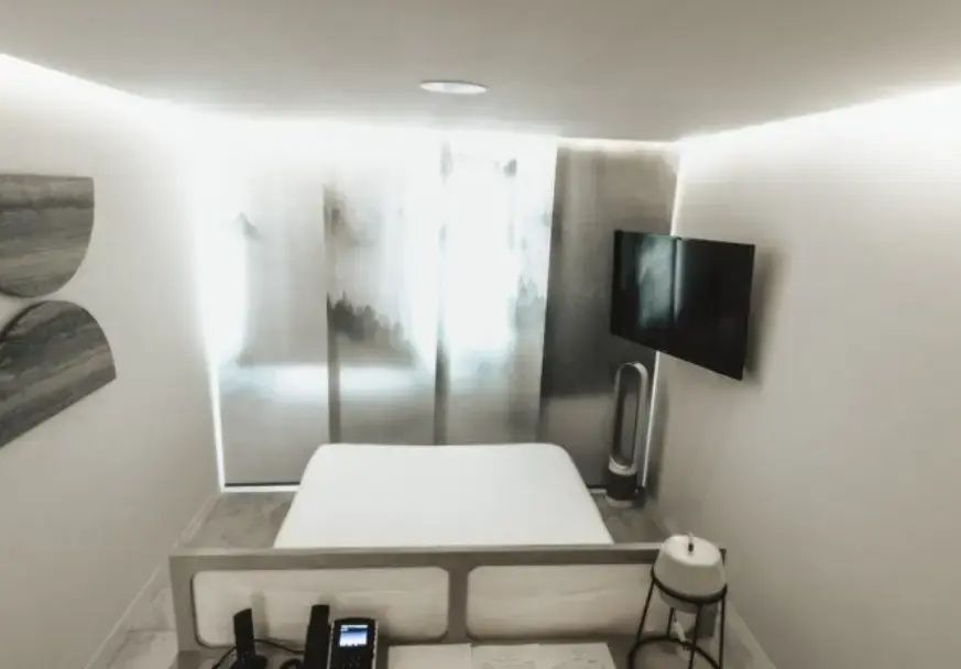 Doppelbett in minimalistischem Hotelzimmer mit Flachbildfernseher an der Wand.