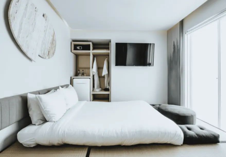 Weißes Bett auf Tatamimatten neben Fernseher und offenem Schrank mit Bademänteln.