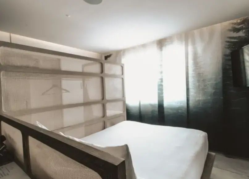 Minimalistisch gestaltetes Hotelzimmer mit weißem Bett und Raumteiler aus Holz.