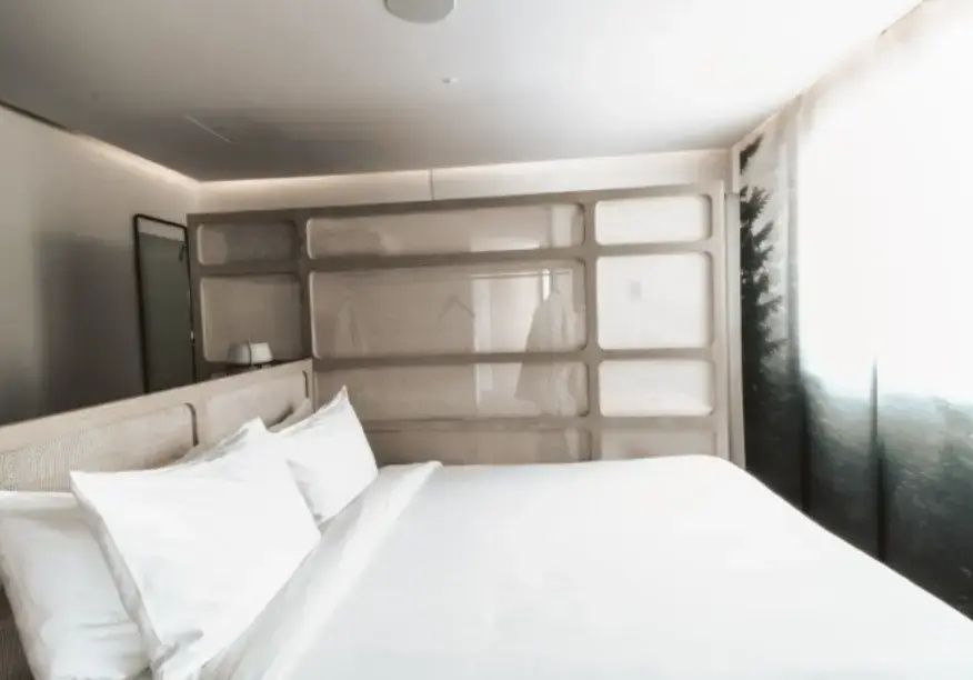 Doppelbett mit weißer Bettwäsche vor einer Schiebewand mit transparenten Feldern.