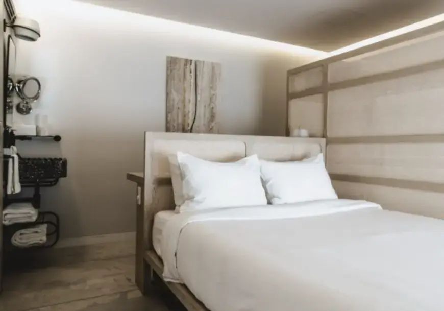 Helles Hotelzimmer mit einem Doppelbett und einer minimalistischen Wand aus Holz.