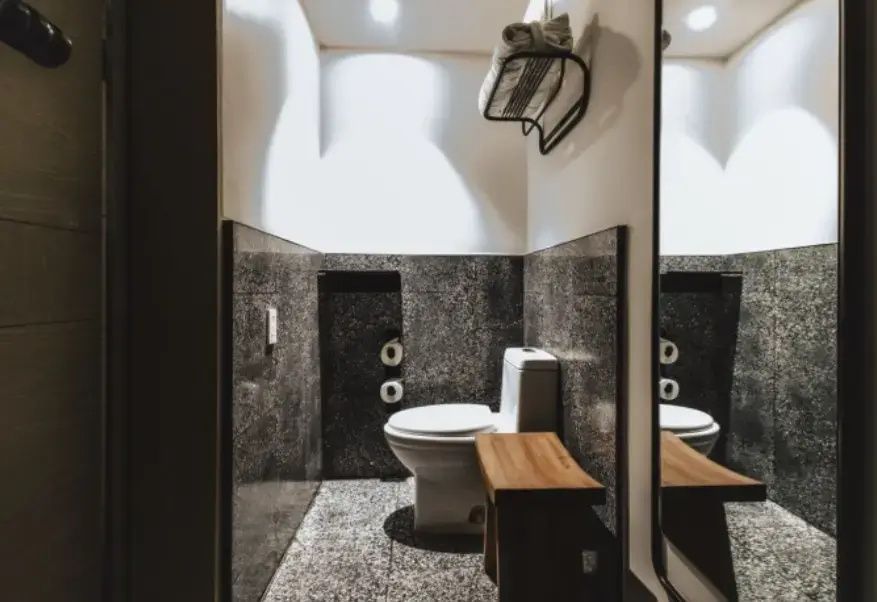 Toilette in einer Nische mit dunklen Granitwänden und einer kleinen Holzbank.