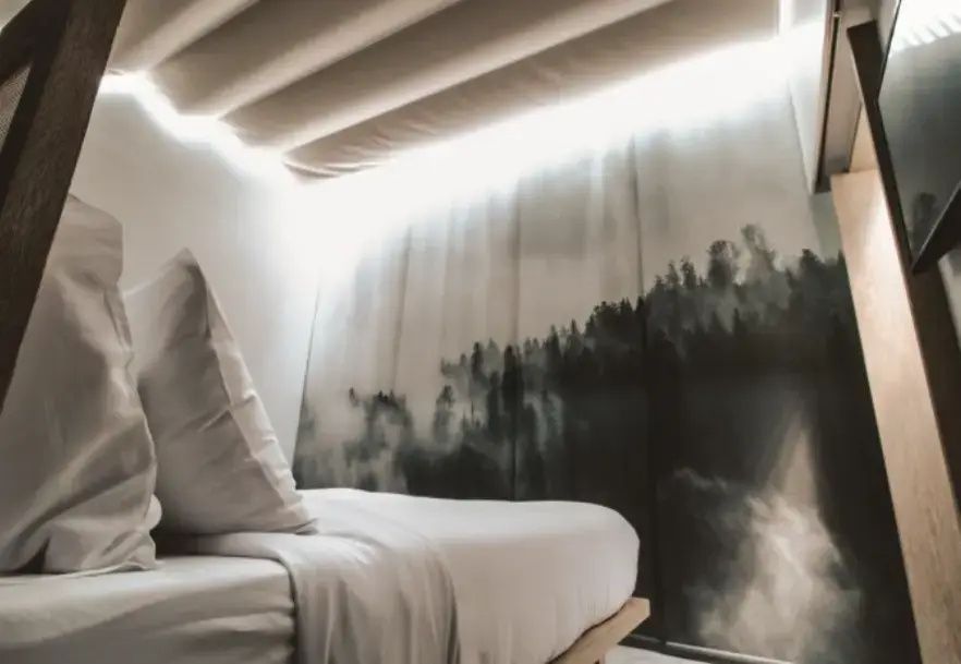 Blick auf ein Bett mit weißer Bettwäsche und dekorativer Wandgestaltung.