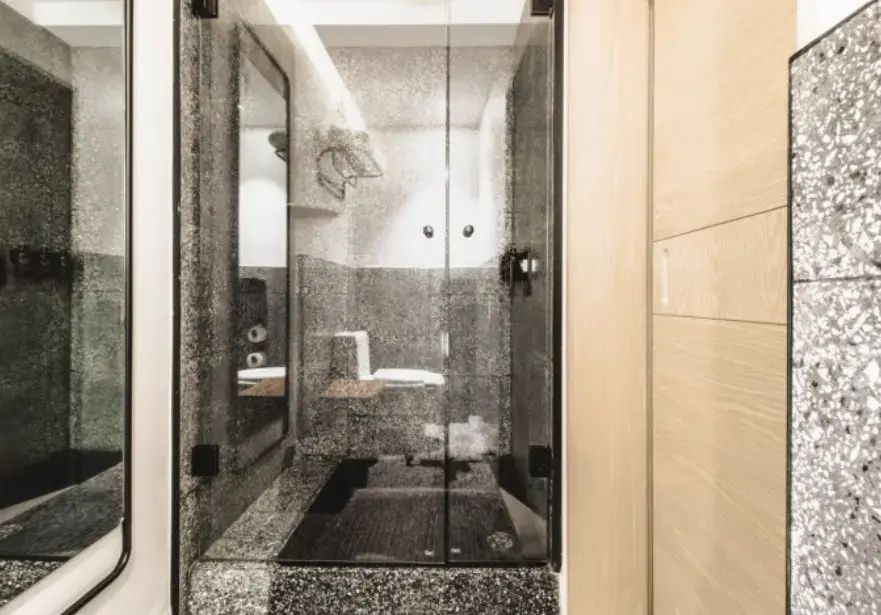 Moderne Dusche mit Glaswand und dunklen Terrazzofliesen im Badezimmer.