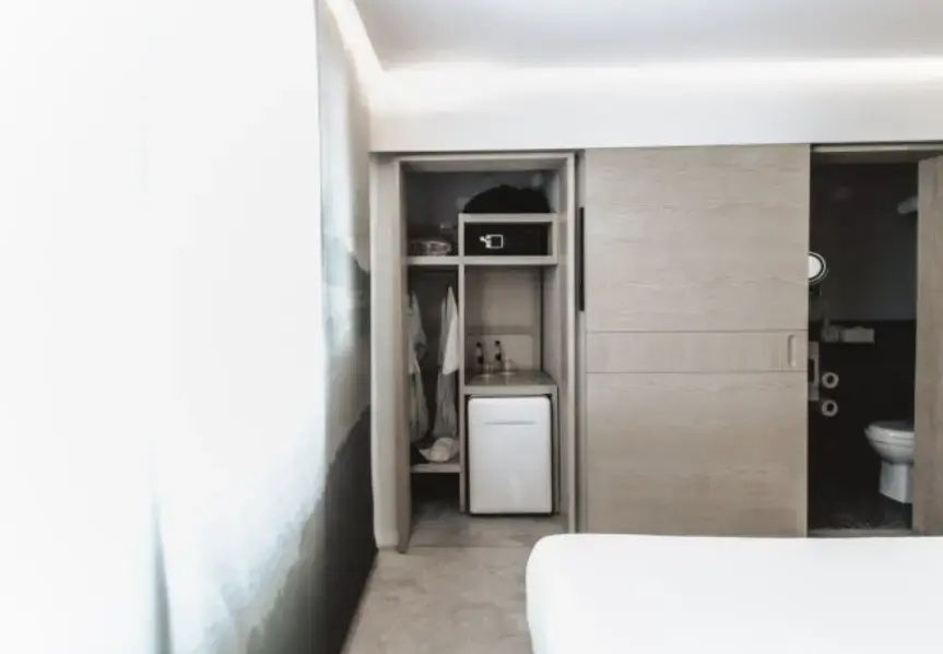 Offener Einbauschrank im Hotelzimmer mit Minibar, Safe und Regalen.
