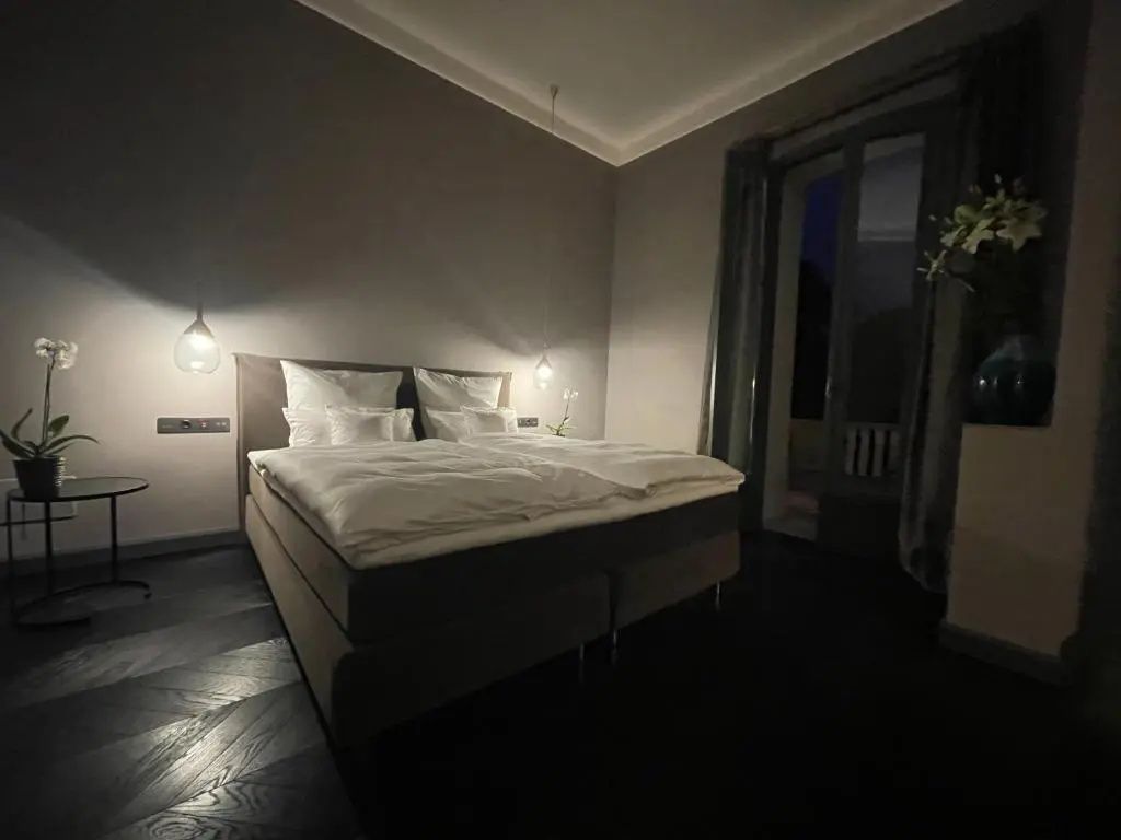 Doppelbett mit weißer Bettwäsche und Hängelampen in einem modern eingerichteten Schlafzimmer.