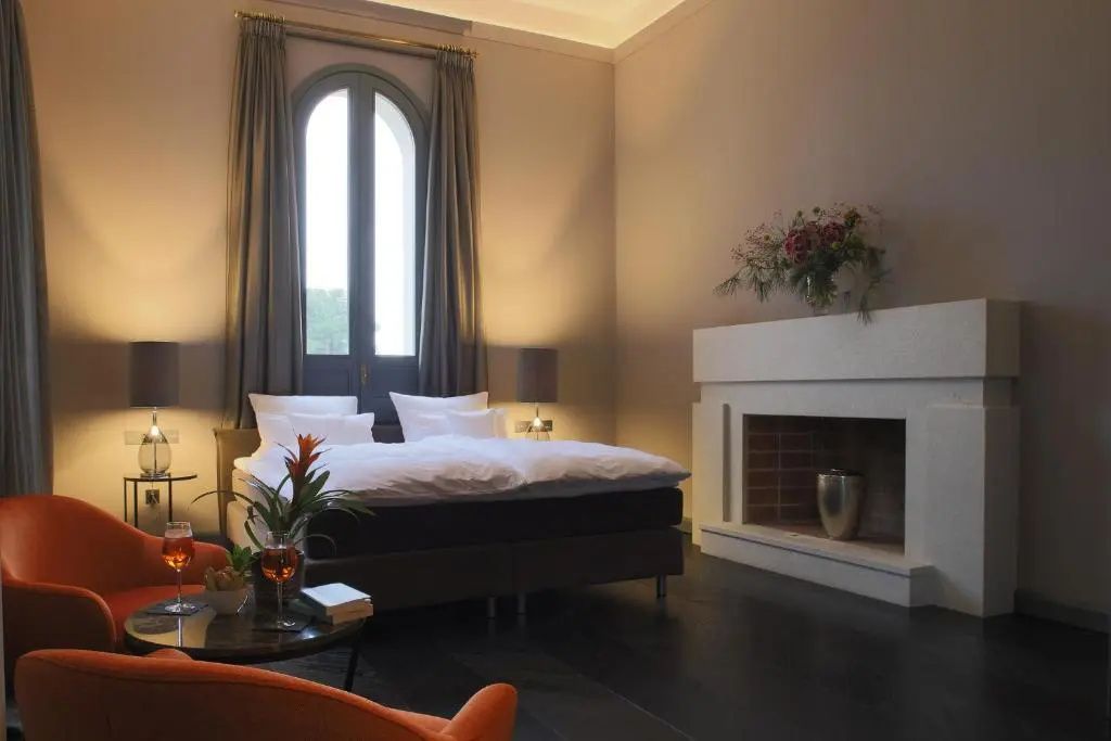 Schlafzimmer mit Doppelbett, einem Kamin, Sitzgelegenheit und hohem Rundbogenfenster.