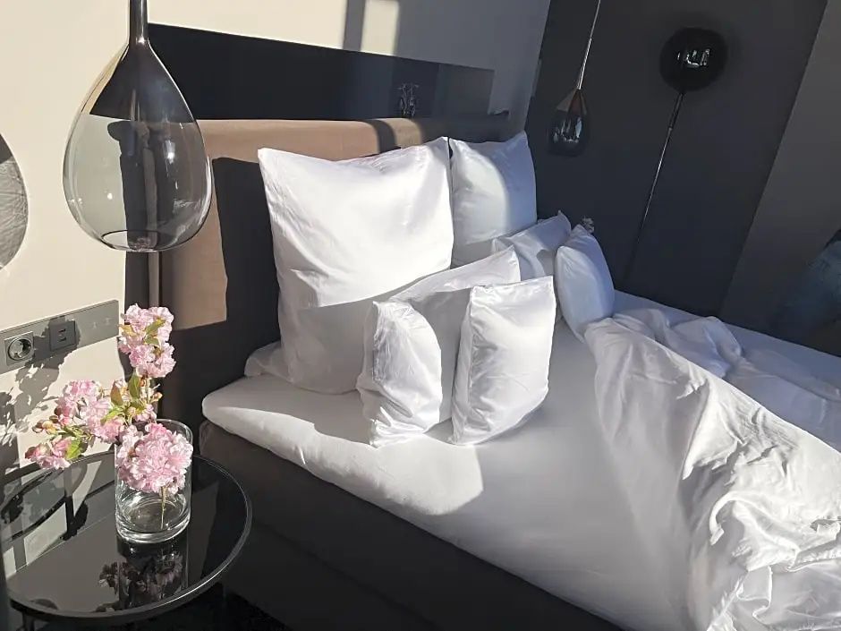 Doppelbett mit weißer Bettwäsche, mehreren Kissen und Beistelltisch mit rosa Blüten.