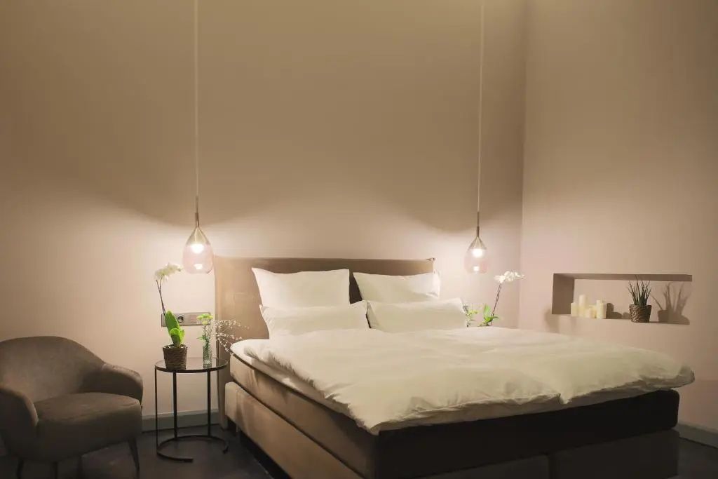 Doppelbett mit weißer Bettwäsche, modernen Hängelampen und Nachttischen mit Orchideen.