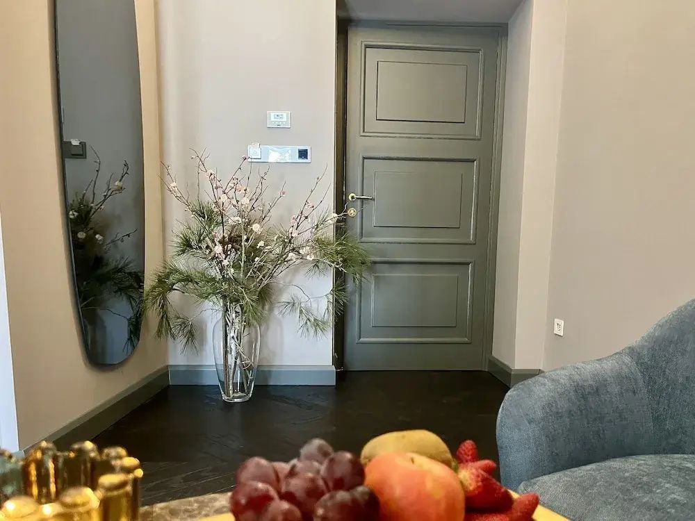 Blick in ein Hotelzimmer mit grauem Türrahmen, Pflanzendekoration und frischem Obst.