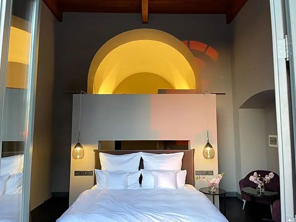 Doppelbett mit weißer Bettwäsche vor einer beleuchteten Bogenkonstruktion