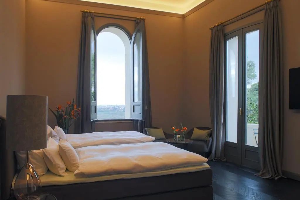 Helles Schlafzimmer mit zwei Betten, Sitzbereich und einem großen Bogenfenster.