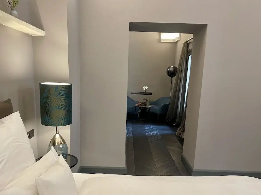 Blick vom Bett durch eine Tür in ein angrenzendes Zimmer mit blauen Sesseln.