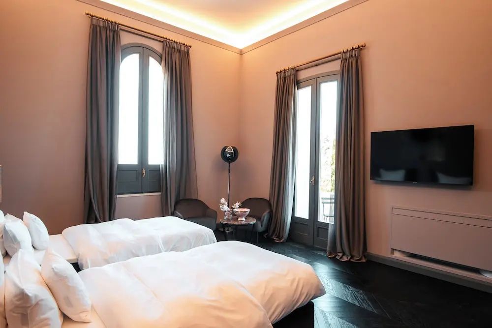 Helles Schlafzimmer mit zwei Betten, Flachbildfernseher und hohem Rundbogenfenster.