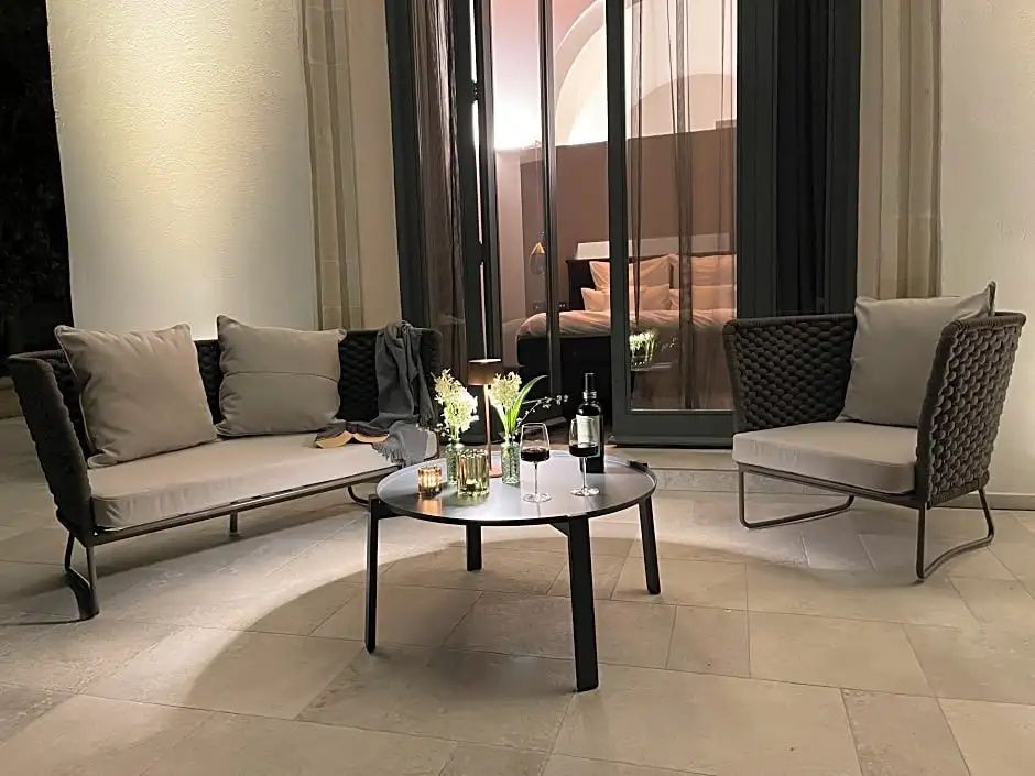 Beleuchtete Terrasse mit Sitzmöbeln und einem Tisch mit Gläsern vor einer verglasten Front.