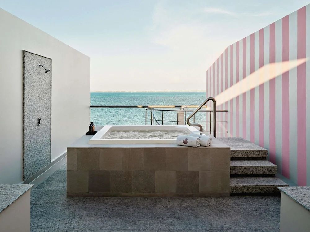Whirlpool auf einer Terrasse mit Blick auf das türkisfarbene Meer und gestreifter Wand.