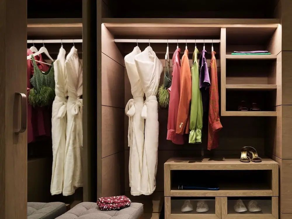 Begehbarer Kleiderschrank aus Holz mit aufgehängter Kleidung und Bademänteln.